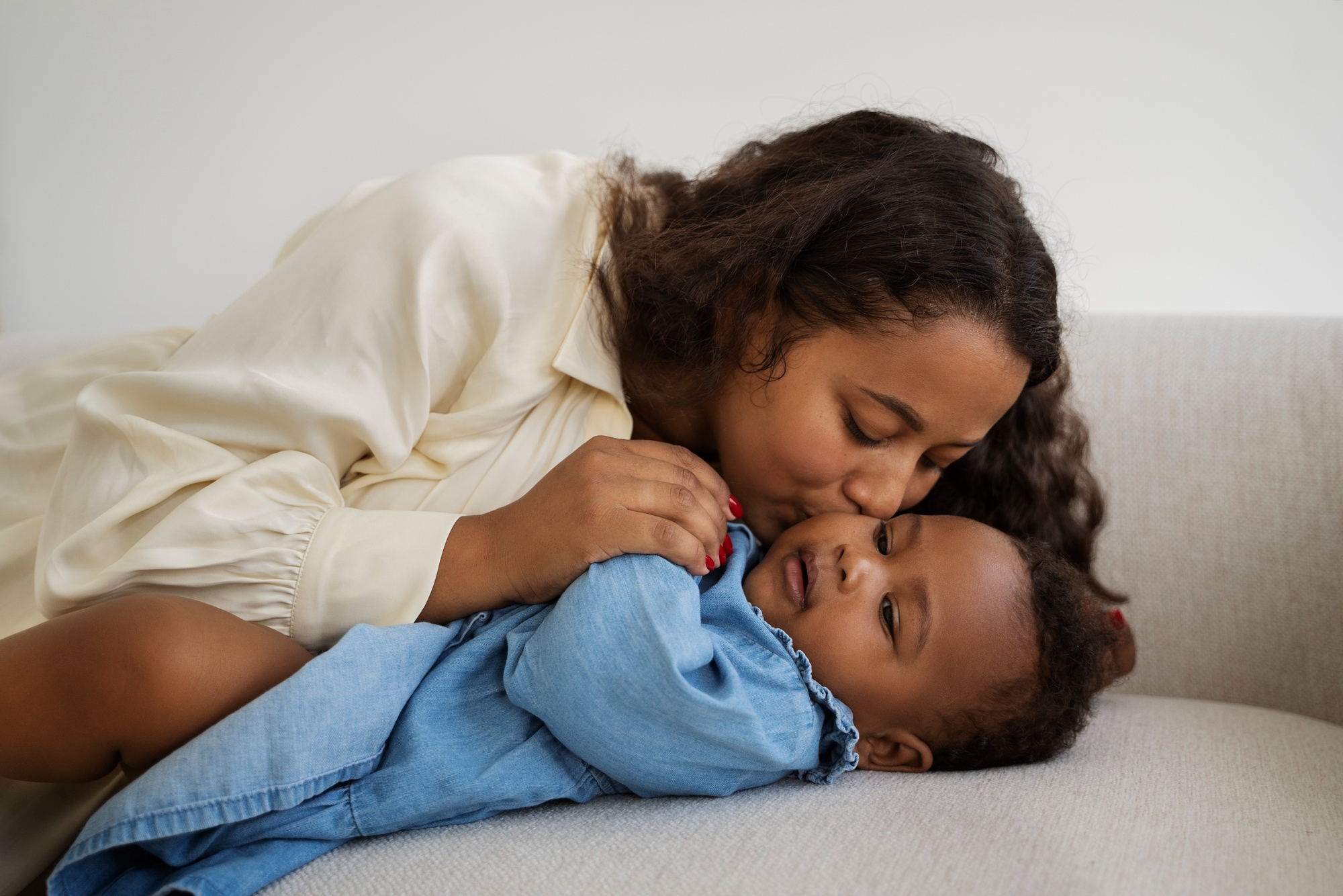 A mother kissing her baby's cheek on a sofa